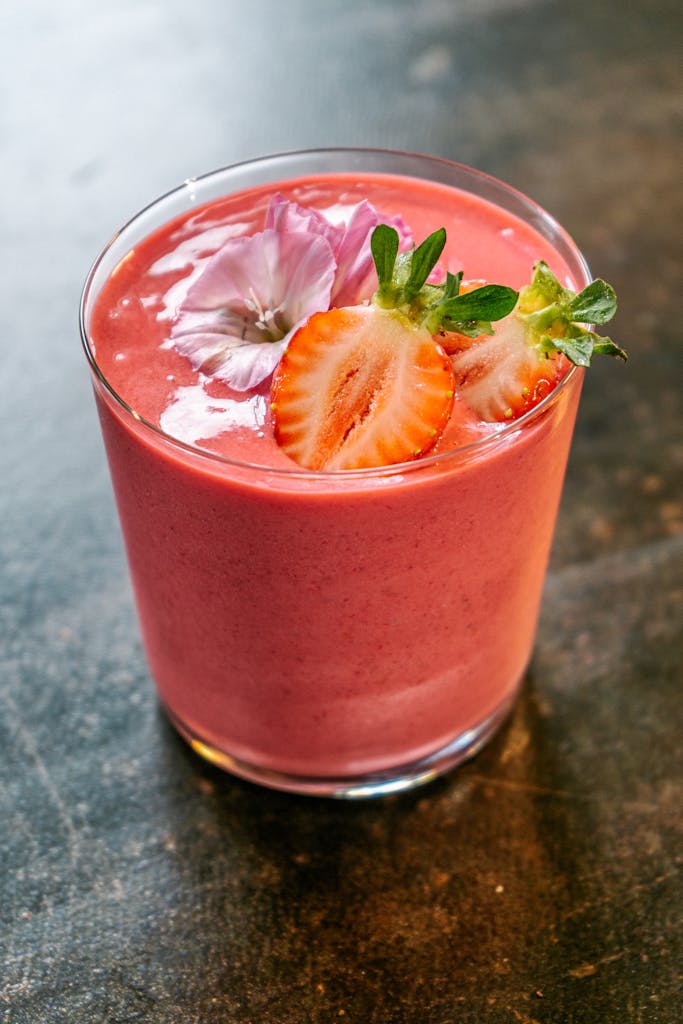 Delicious strawberry smoothie garnished with fresh flower and strawberry slice in a glass.