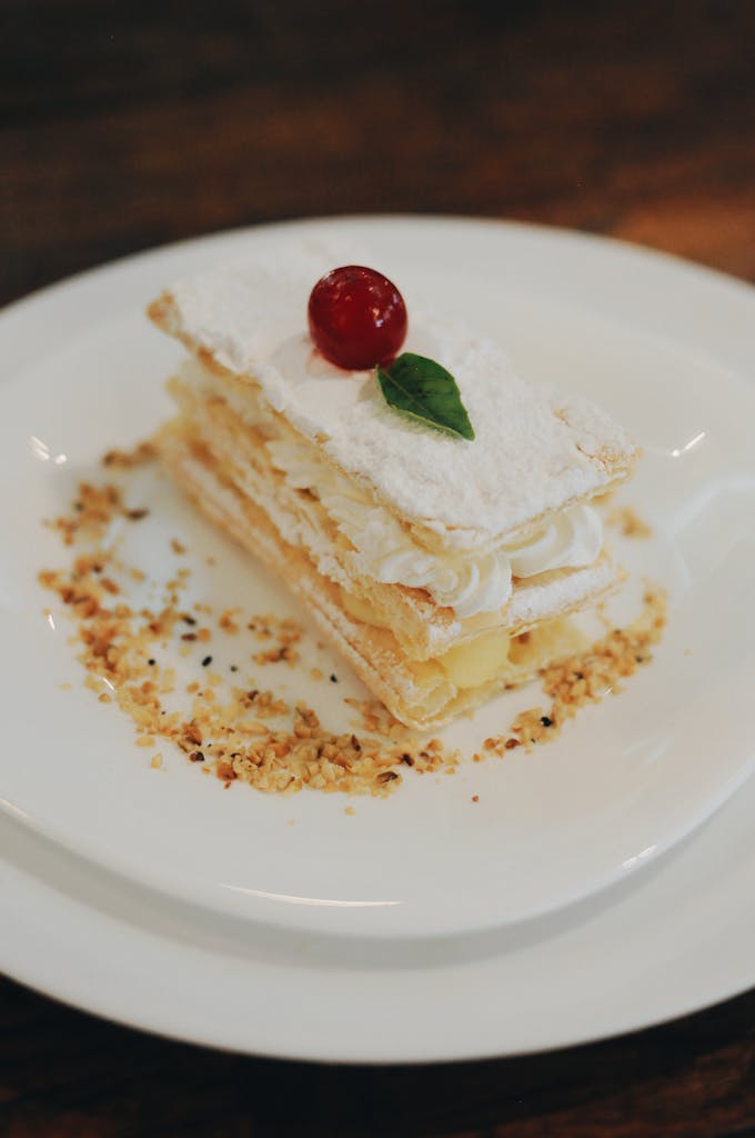 Indulge in a creamy layered pastry topped with a cherry and garnished with nuts.