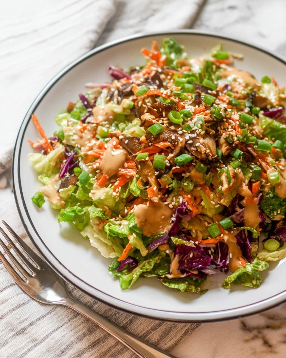 A colorful salad sits on a white plate with a thin black rim, featuring a mix of layers that include chopped green lettuce and purple cabbage strips at the base, shredded orange carrots scattered throughout, and small pieces of grilled brown mushrooms mixed in. There are also chopped green onions sprinkled on top, with a drizzle of creamy light brown dressing and a light scattering of sesame seeds. The salad appears fresh and textured, set against a white marbled surface with a silver fork partially visible next to the plate. Photo taken with an iphone --ar 4:5 --v 7