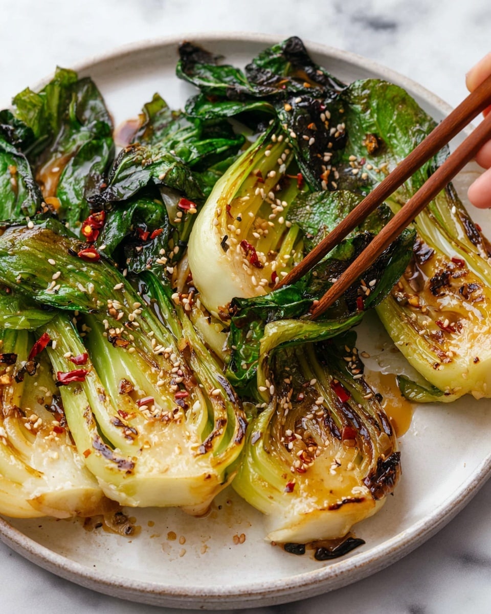 A white plate holds several pieces of cooked bok choy, each cut in half showing their thick, pale green stems layered below dark green, slightly wilted leaves. The bok choy has a shiny, caramelized surface with browned edges and some char marks, giving a glossy texture. Small white sesame seeds and bits of red chili flakes are sprinkled over the vegetables. A pair of brown wooden chopsticks, held by a woman's hand, pick up one piece of bok choy from the plate. The background is a white marbled texture. photo taken with an iphone --ar 4:5 --v 7
