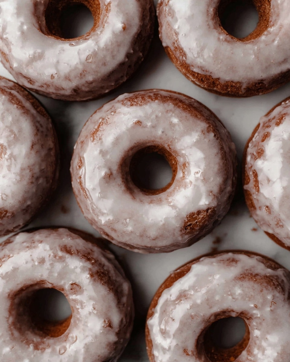 A close-up top view of seven brown glazed donuts arranged tightly on a white marbled surface, each donut showing a smooth shiny white glaze coating with some drip marks and small cracks. The donuts have a slightly rough texture underneath the glaze with classic circular holes in the center. The lighting highlights the glaze’s glossy finish and the donuts' soft, cake-like texture beneath. Photo taken with an iphone --ar 4:5 --v 7