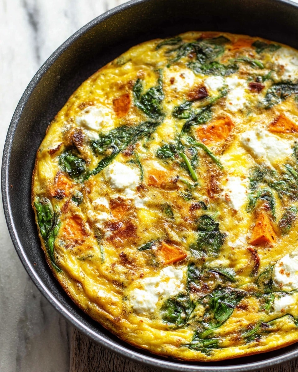 A frittata cooked in a dark pan with a golden-yellow egg base showing a slightly browned, firm texture around the edges and softer in the middle, topped with scattered dollops of white cheese, bright green leafy spinach mixed in, and chunks of orange sweet potato spread evenly throughout. The surface glistens lightly with oil and has a rustic, home-cooked look. The pan rests on a white marbled texture. Photo taken with an iphone --ar 4:5 --v 7