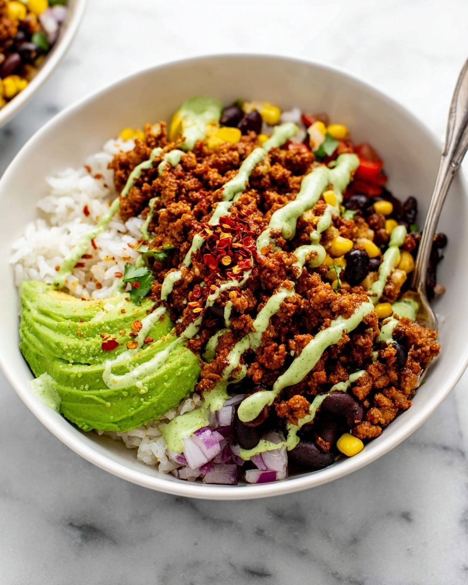 A white bowl filled with four visible layers: the bottom layer is white rice with a soft texture, the second layer is bright green sliced avocado on one side, the third layer is a mix of cooked corn kernels, black beans, and diced red onions on the other side, and the top layer is crumbled, browned seasoned ground meat spread over the middle. The dish is finished with light green sauce drizzled in thin stripes across the top and a few red chili flakes scattered over the seasoned meat. A spoon is placed inside the bowl, and the bowl rests on a white marbled surface. photo taken with an iphone --ar 4:5 --v 7