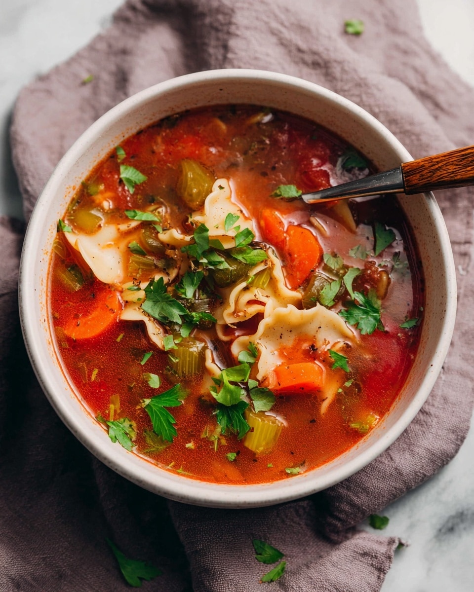 A white bowl filled with rich, red tomato broth containing three main layers: bright orange carrot slices and light green celery pieces at the bottom, soft, curly-edged beige pasta pieces in the middle, and fresh, bright green parsley leaves scattered on top; a wooden-handled spoon resting inside the bowl, all placed on a soft gray cloth with a white marbled surface underneath. photo taken with an iphone --ar 4:5 --v 7