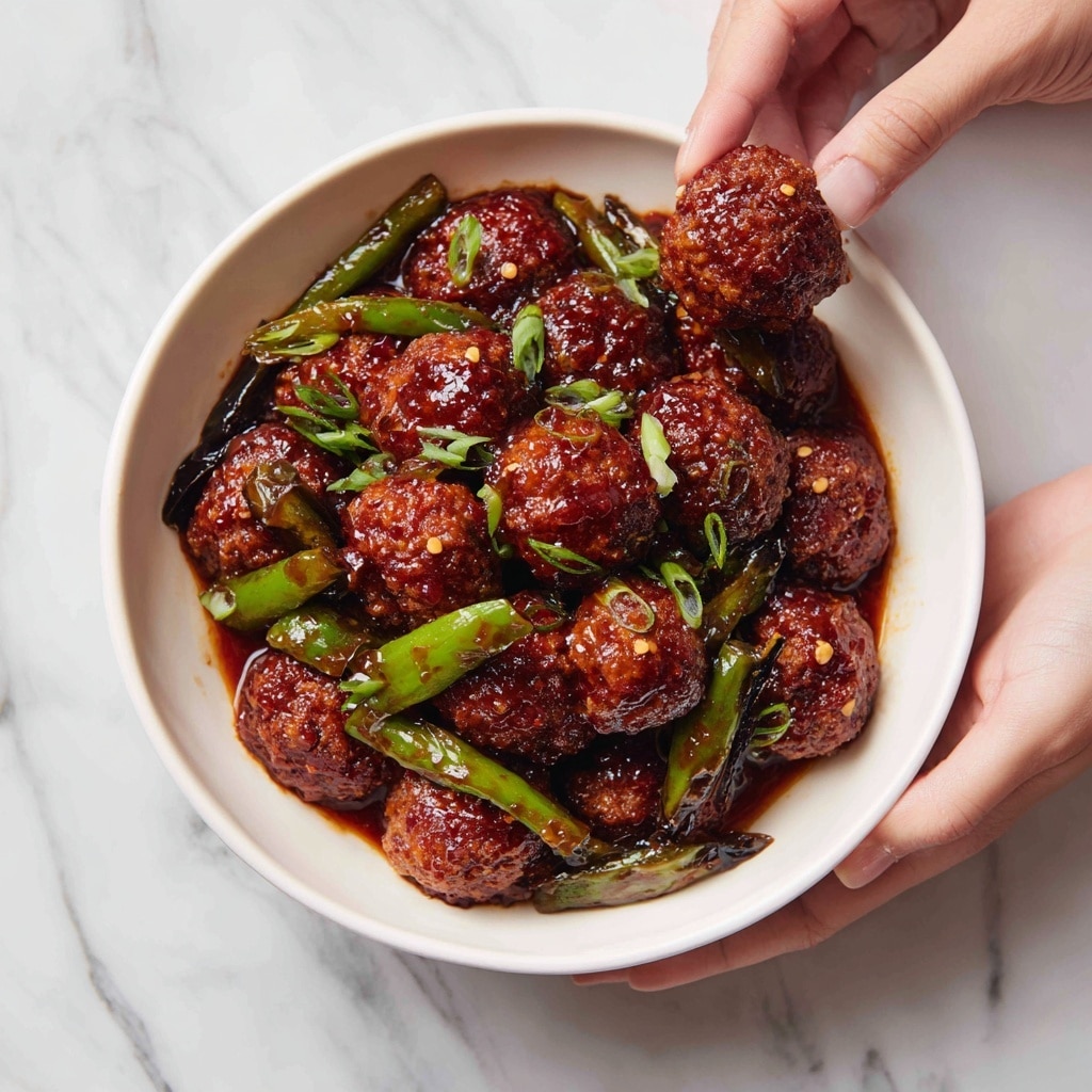 A round white bowl filled with multiple deep reddish-brown fried vegetable balls covered in shiny sauce, mixed with cooked green bell pepper strips and chopped spring onions scattered on top. The vegetable balls are arranged closely, showing a slightly rough texture with a crispy coating. Two woman's hands hold the bowl from the sides, while a third woman's hand is holding one sauced ball above the bowl. The bowl is placed on a white marbled surface. photo taken with an iphone --ar 4:5 --v 7