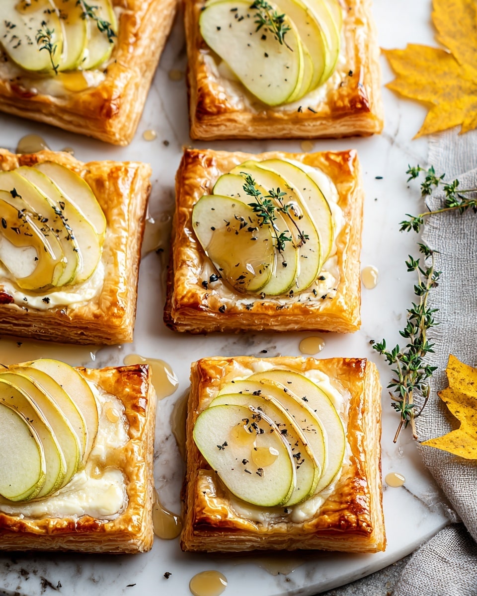 The image shows six square pastries with golden brown, flaky layers forming the base and edges. Each pastry has two thin, pale green and yellow apple slices arranged on top, resting on a smooth, creamy white cheese layer. Small green sprigs of thyme and black pepper dots add a fresh and textured look over the apples. A shiny, light amber syrup is drizzled generously across the pastries and pooling slightly on the white marbled surface beneath them. Yellow autumn leaves and small thyme sprigs float on the right side, next to a gray cloth. photo taken with an iphone --ar 4:5 --v 7