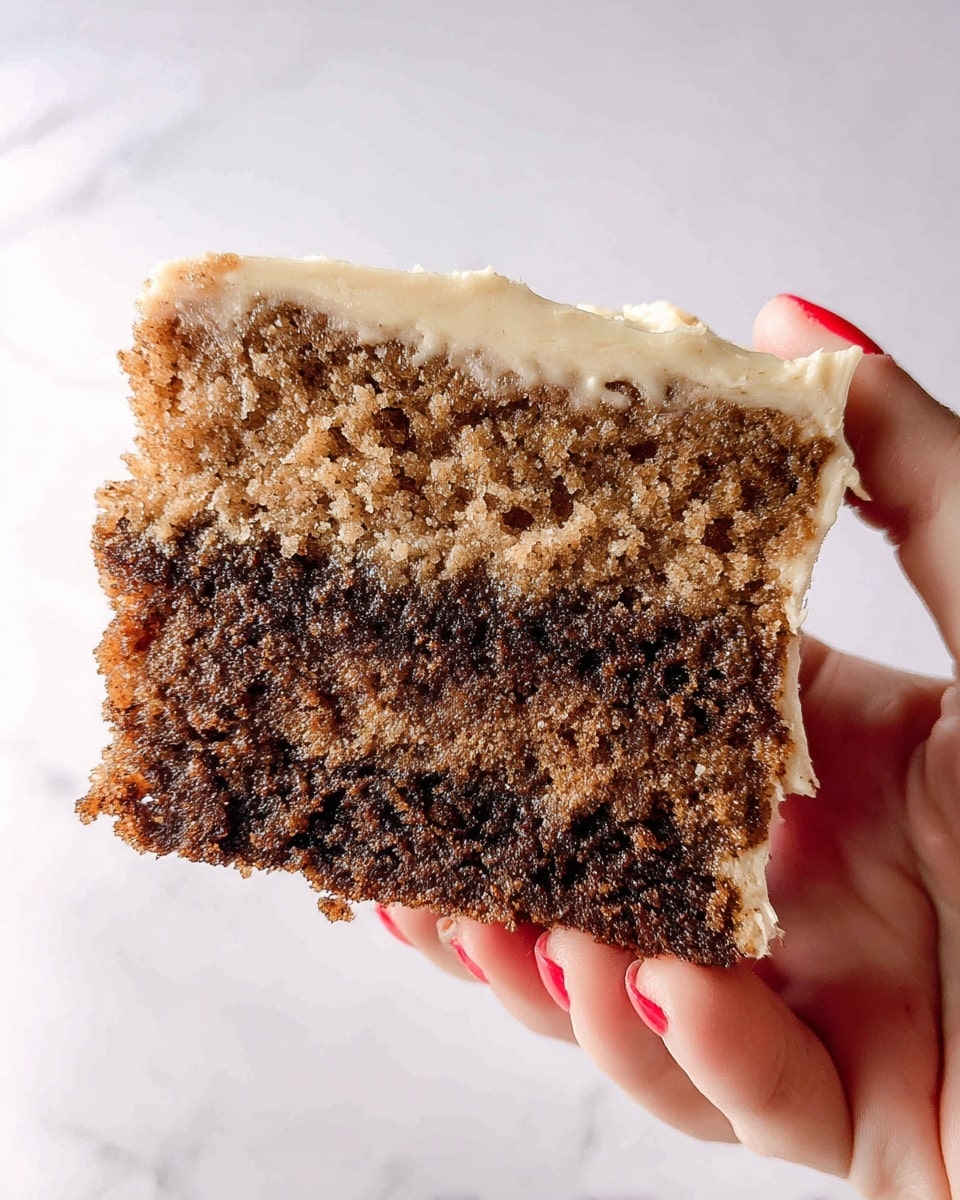 A close-up of a slice of layered cake held by a woman's hand with red nail polish, showing three distinct layers: the bottom and middle layers are a rich, dark brown cake with a moist texture, the top layer is a lighter, tan-colored cake, slightly crumbly, and the top surface is covered with a creamy, beige icing that appears smooth and thick. The background is a white marbled texture. photo taken with an iphone --ar 4:5 --v 7