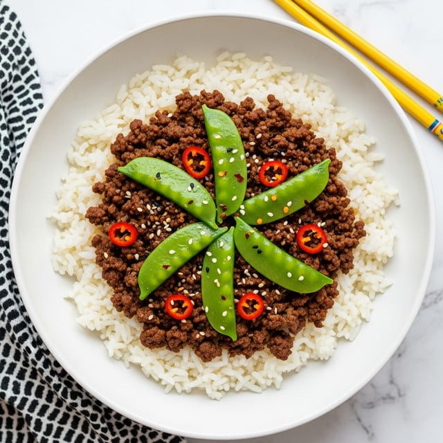 A white bowl holds a base layer of fluffy white rice spread evenly, topped by a thick layer of dark brown minced beef cooked with visible spices, sprinkled with red chili flakes and sesame seeds. On top of the beef, six bright green snap pea pods are placed in a loose circular pattern, adding a fresh texture and color contrast. The bowl sits on a white marbled surface, with a pair of yellow chopsticks on the top right and a black and white patterned cloth partially visible at the bottom left. Photo taken with an iphone --ar 4:5 --v 7