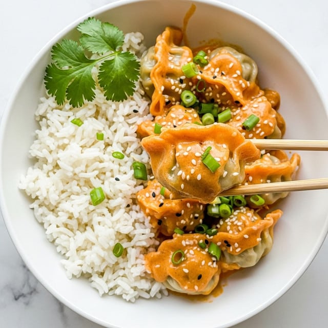 A white bowl contains a dish with two main parts: on the right, a heap of white fluffy rice with visible grains, and on the left, four golden-brown dumplings covered in a thick, creamy orange sauce. The sauce has a smooth texture and lightly coats the dumplings and rice edges. The dumplings show slight browning on their edges, indicating they are cooked. Green sliced scallions and fresh green cilantro leaves are scattered on top, adding color contrast. Light sesame seeds sprinkle the dish. Two light wooden chopsticks hold one dumpling in the center of the bowl. The bowl is set on a white marbled surface. Photo taken with an iphone --ar 4:5 --v 7
