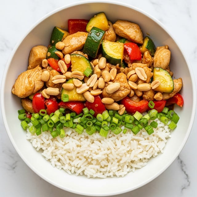A white bowl filled with three layers: at the bottom, a base of fluffy white rice with a soft texture; the middle layer has chunky pieces of cooked chicken and diced green zucchini, stir-fried with red bell pepper pieces, all coated in a shiny, sticky brown sauce; the top layer is sprinkled with chopped green onions and a generous amount of whole and broken light brown peanuts, adding a crunchy texture. The bowl sits on a white marbled surface. photo taken with an iphone --ar 4:5 --v 7