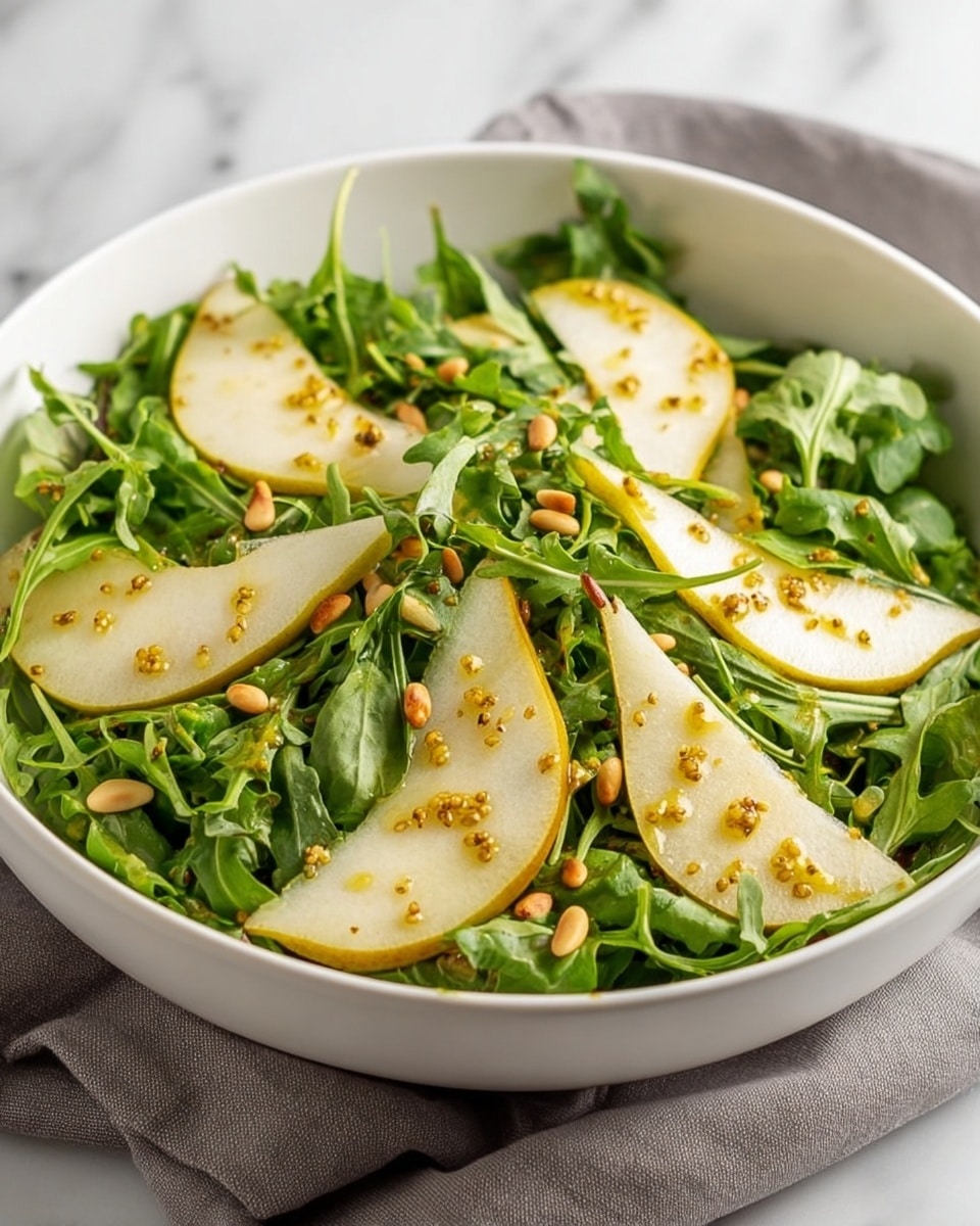 A white bowl filled with a fresh salad consisting of a bed of bright green arugula leaves as the base layer, topped with thin, curved slices of light yellow pear arranged evenly around the bowl. The pear slices are slightly translucent with a smooth texture. Scattered on top are small, light beige pine nuts adding a crunchy texture, and the entire salad is drizzled with a glossy golden brown grainy mustard dressing, giving a shiny look to the ingredients. The bowl is on a neatly folded gray cloth on a white marbled surface. Photo taken with an iphone --ar 4:5 --v 7