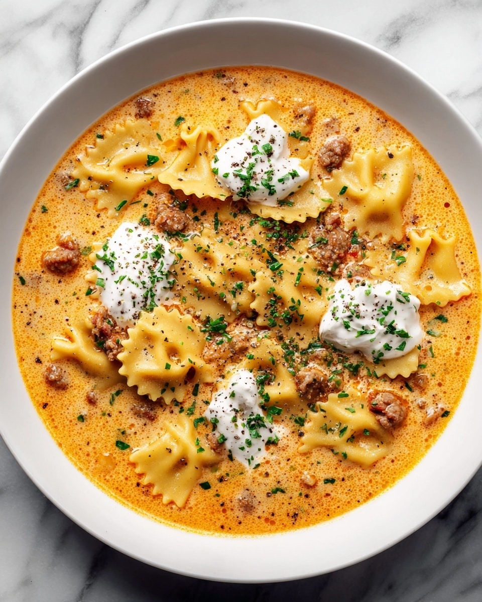 A white bowl filled with a creamy soup that has several wide, curved pasta pieces floating in a light orange broth. There are small chunks of browned ground meat scattered throughout the soup, adding a textured look. On top, three dollops of smooth white cream are placed near the center, each sprinkled lightly with ground black pepper. Small green herb leaves are scattered around for color contrast. The bowl rests on a white marbled surface. photo taken with an iphone --ar 4:5 --v 7