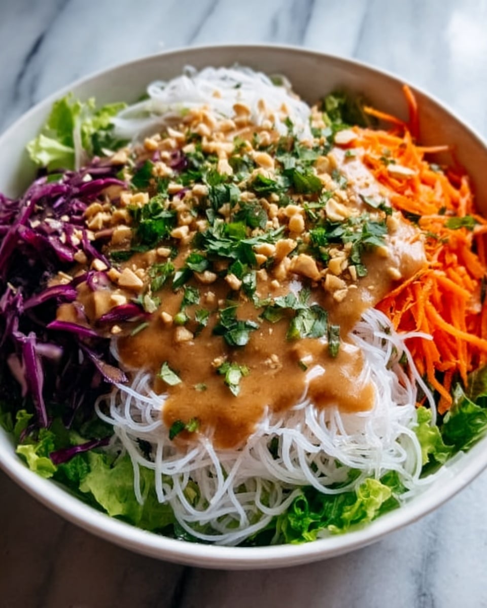 A white bowl filled with layers of fresh salad: the bottom layer is green leafy lettuce, topped with thin white rice noodles in the center. Around the noodles, there are colorful sections of purple cabbage on the left and shredded orange carrots on the right. A creamy light brown dressing is drizzled over the noodles and some chopped green herbs scattered on top. The bowl is placed on a white marbled surface. Photo taken with an iphone --ar 4:5 --v 7