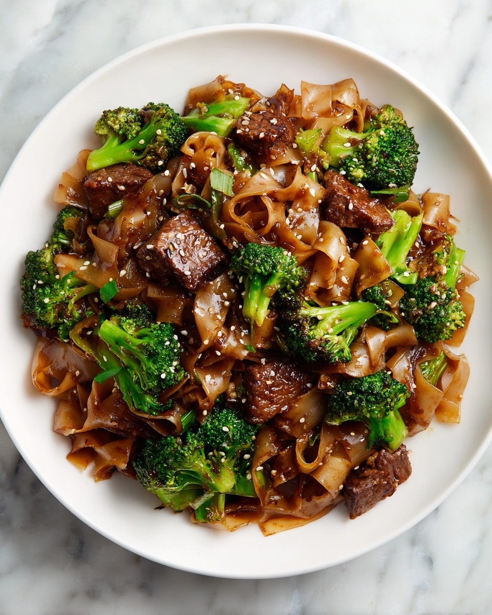 A white plate holds a serving of stir-fried wide rice noodles that are light brown and soft-looking, mixed with green broccoli florets scattered evenly throughout. There are several pieces of browned beef chunks placed on top and hidden among the noodles, coated in a shiny dark brown sauce. Small pieces of garlic and sesame seeds are sprinkled over everything, adding texture and variation. The dish looks glossy and well-cooked, sitting on a white marbled surface. Photo taken with an iphone --ar 4:5 --v 7