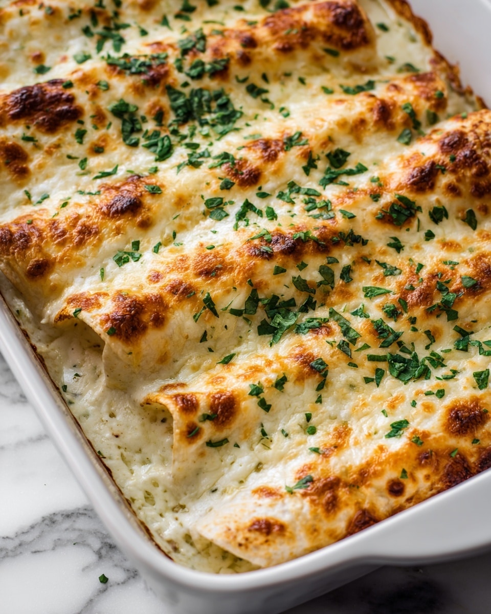 The image shows a close-up of three rolled enchiladas placed side by side in a dark baking dish. Each enchilada is covered with a thick, creamy white sauce that is golden brown and slightly bubbly on top, indicating it has been baked. Fresh chopped green herbs, likely cilantro or parsley, are sprinkled evenly over the sauce, adding a touch of bright green color. The dish sits on a white marbled surface with a soft focus on the background. Photo taken with an iphone --ar 4:5 --v 7