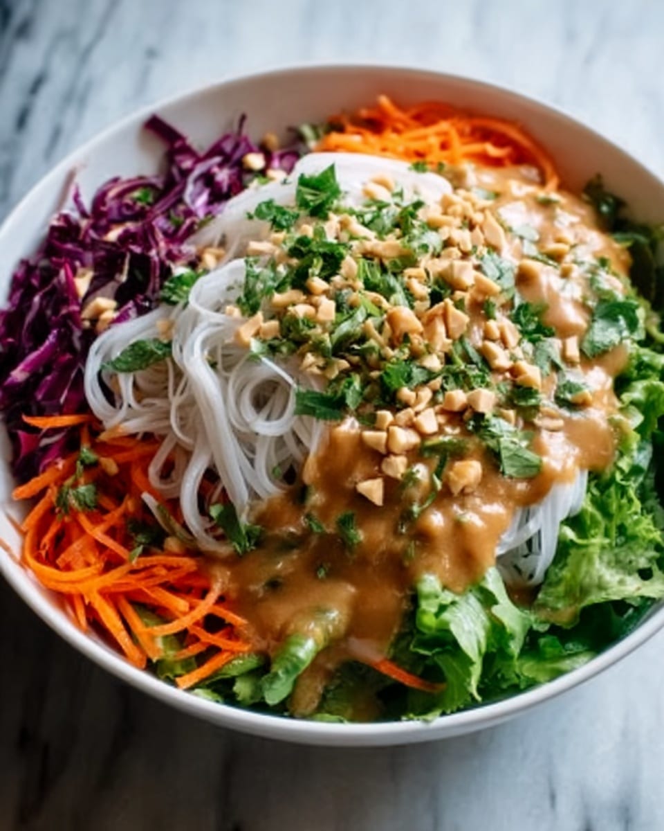 A white bowl filled with a colorful salad, showing several layers: at the base, a bright green layer of lettuce, topped with white thin rice noodles placed in the center, on the left side thin strips of purple cabbage, and on the right side thin orange carrot strips. The salad is covered with a thick, creamy light brown sauce drizzled evenly on top. Chopped green herbs and crushed nuts are sprinkled over the entire dish, adding texture. The bowl is set on a white marbled surface. Photo taken with an iphone --ar 4:5 --v 7