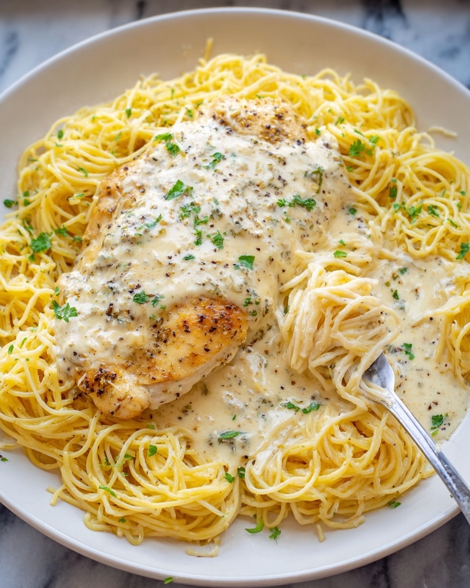A white plate filled with a bed of thin yellow spaghetti noodles arranged in a loose circular shape. On top, there is a large grilled chicken breast covered with a creamy white sauce that looks rich and smooth, speckled with black pepper and small green parsley leaves scattered over both the chicken and noodles. A silver fork is twirling some of the creamy noodles on the right side of the plate. The plate is set on a white marbled surface. photo taken with an iphone --ar 4:5 --v 7