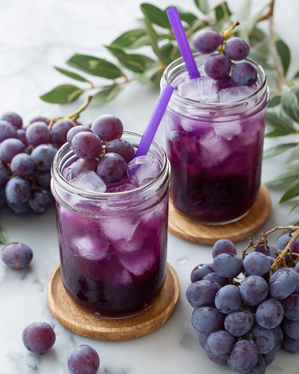 Two clear glass jars filled with purple grape drink and ice cubes sit on a white marbled surface, each with a purple straw in them. The drink is deep purple and topped with several whole dark purple grapes floating on top. Around the jars, small bunches of dark purple grapes lay scattered on the white marbled texture. The jars have a round orange coaster underneath. In the background, blurred lemons and green leaves add soft color. Photo taken with an iphone --ar 4:5 --v 7