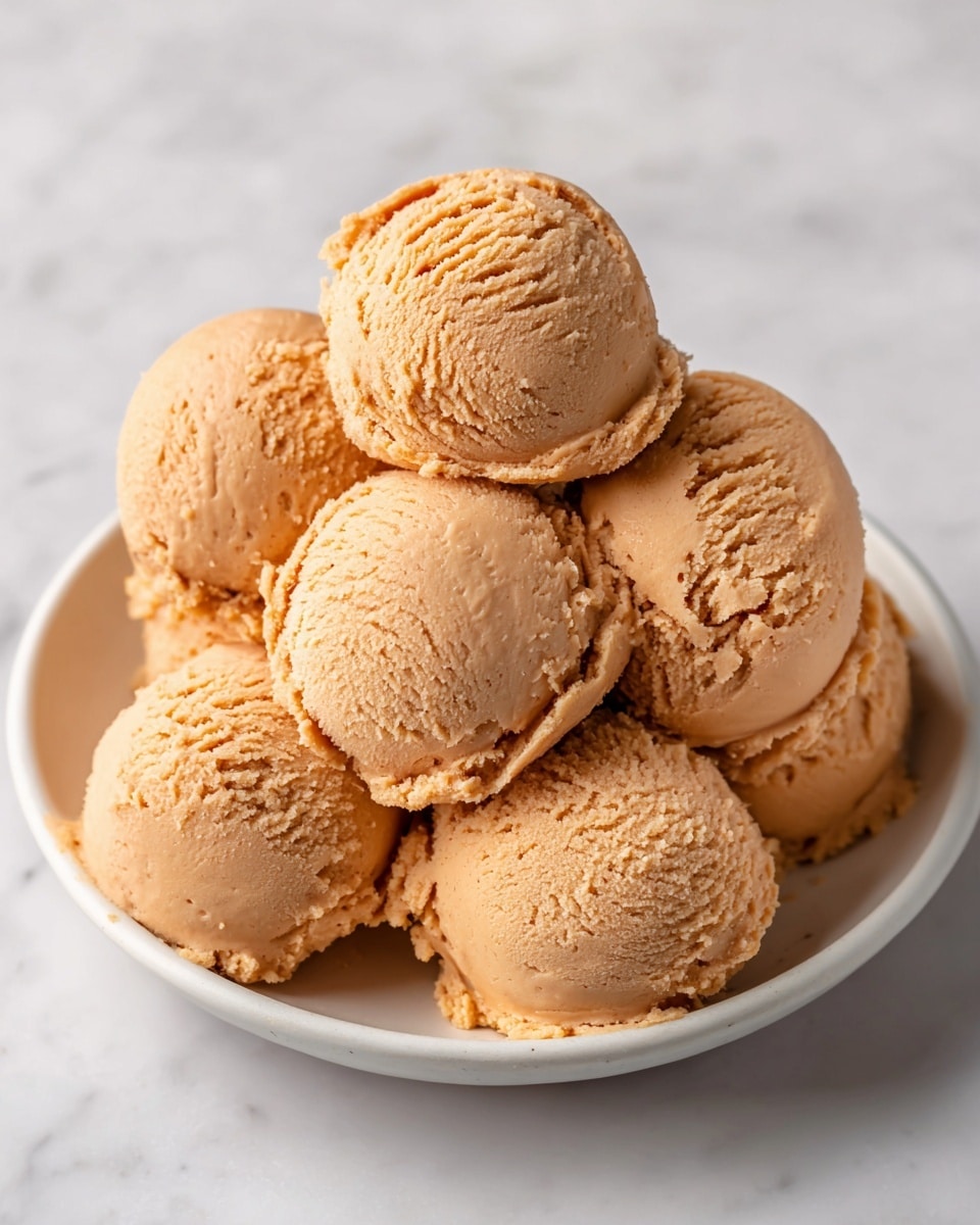 A white bowl filled with eight round scoops of smooth, creamy brown peanut butter, stacked lightly on top of each other, each scoop showing soft texture and small ridges from scooping, placed on a white marbled surface with soft natural light casting gentle shadows behind the bowl, giving warm and cozy feeling, photo taken with an iphone --ar 4:5 --v 7
